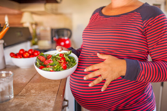 Pregnant Caucasian mother holding salad in kitchen