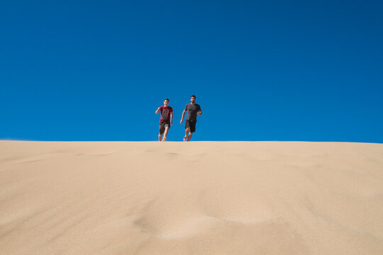 Caucasian father and son running on sand dune