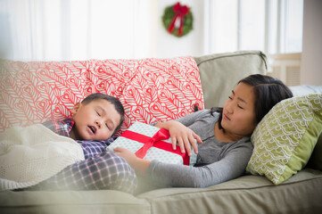 Asian brother and sister napping on sofa with Christmas gift