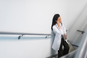 High angle view of stressed mixed race doctor standing on staircase