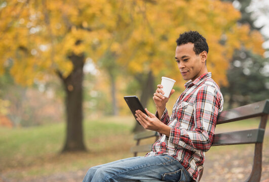 Mixed race man using digital tablet on park bench