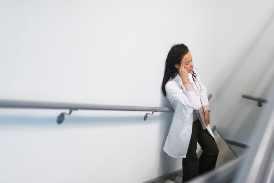 High angle view of stressed mixed race doctor standing on staircase