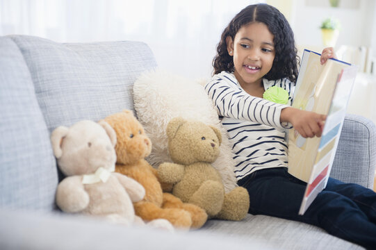 Mixed race girl teaching teddy bears on sofa