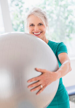 Older Caucasian woman holding exercise ball in gym