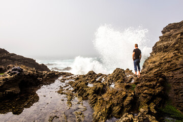 Caucasian hiker watching crashing ocean waves