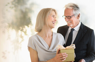 Smiling older Caucasian man giving wife a gift