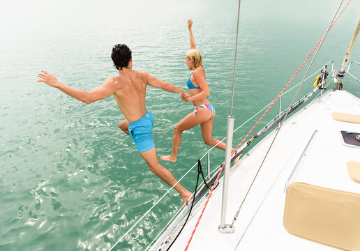 Couple jumping from sailboat deck into ocean
