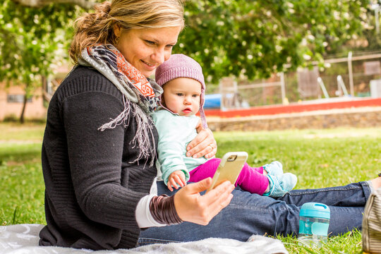 Caucasian mother and baby daughter using cell phone in park