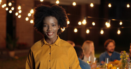 Portrait of young beautiful African American woman smiling cheerfully and standing at outside party...