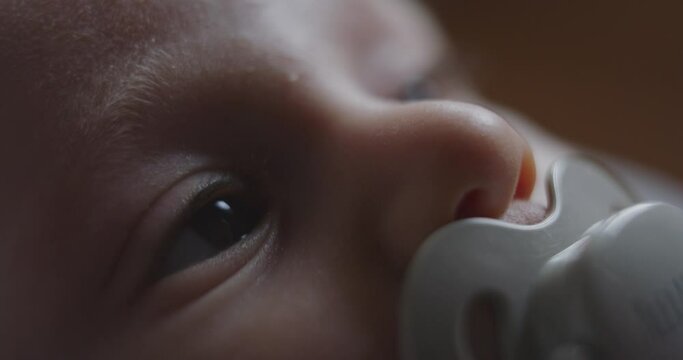Cinematic macro shot of a cute newborn baby with pacifier is looking around while lying in a crib before asleep in a nursery. Concept of children, baby, parenthood, childhood, life.