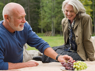 Older couple eating grapes at picnic in park