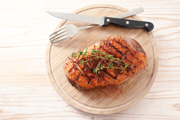 Crispy grilled duck breast with rosemary garnish on a wooden cutting board with fork and knife,...