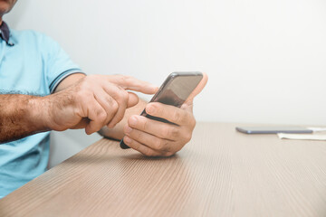 Using a mobile phone. The man uses the smartphone while sitting at the desk.