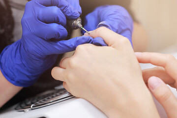 Close Up shot of hardware manicure in a beauty salon. Manicurist in protective gloves is applying electric nail file drill to manicure on female fingers.