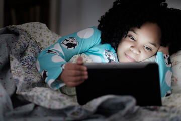African American girl using digital tablet in bed