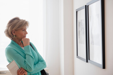 Older Caucasian woman examining artwork in gallery