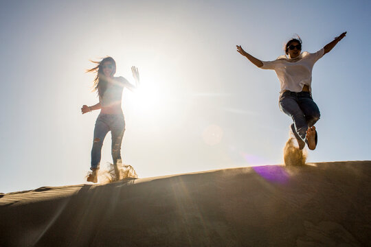 Mixed race women playing in sand dunes