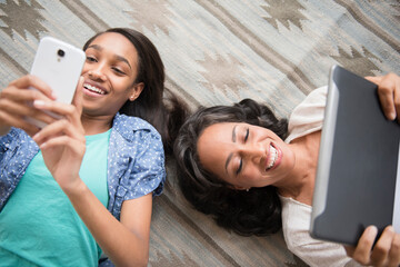 Mother and daughter laying on carpet using cell phone and digital tablet