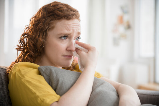 Crying Caucasian woman clutching pillow wiping tears