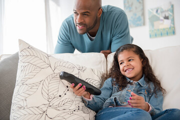 Father and daughter watching television on sofa,