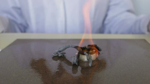 Chemical reaction of Pharaoh's serpent demonstration: conversion of Calcium gluconate to Hexamine fuel tablet. Snakes of black ash rise from the fire. Medium shot, real time, contains people, educatio