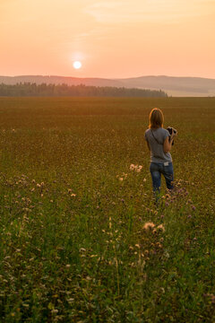 Caucasian woman walking in field at sunset with camera
