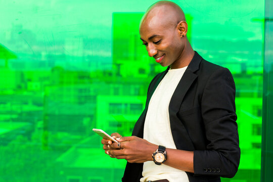 Smiling gay Black man texting near green window