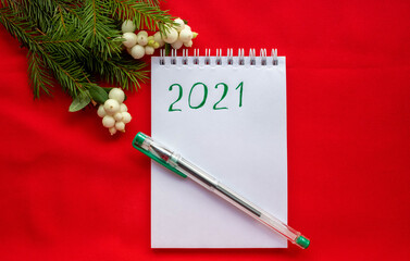 New year's composition.Notepad with a pen and spruce branches with white berries on a red background