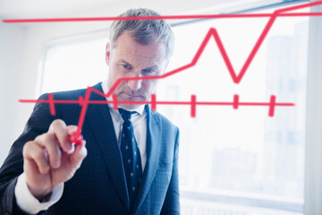 Older Caucasian businessman drawing chart on glass wall