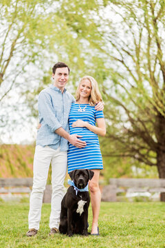 Smiling Caucasian man and expectant mother posing with dog in park