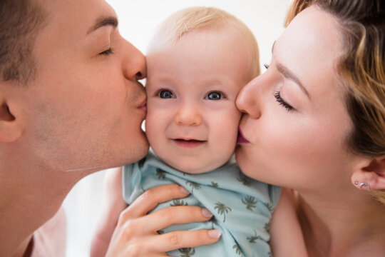 Caucasian mother and father kissing cheeks of baby son
