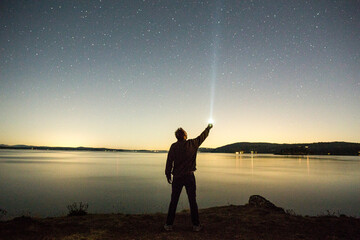Caucasian man pointing flashlight at night sky near water