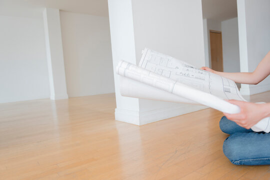 Hispanic woman sitting on floor of empty apartment holding blueprint