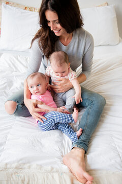 Caucasian mother sitting on bed holding twin baby daughters