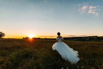 Portrait of beautiful bride in long white wedding dress walking at sunset outdoors.  woman in long wedding gown dress on the grass in summer back view. wedding day. girl in long white dress on nature