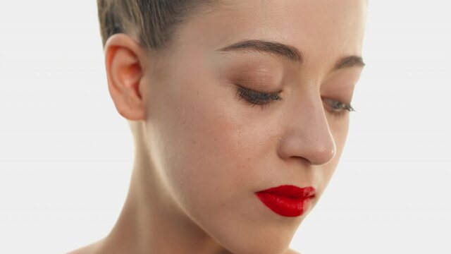 Model looking down and holds fingers on her cheek. Profile of young girl with natural beauty, ligth makeup and bright red lipstick. Concept of spa treatments for beauty, cosmetics, base makeup.