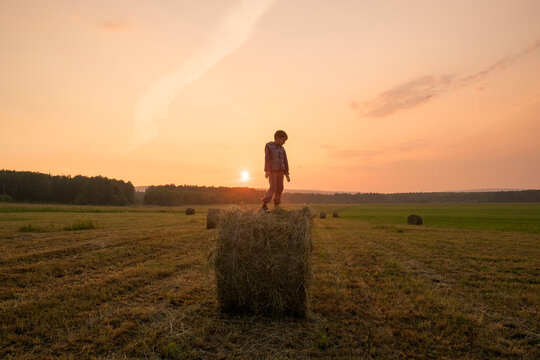 Mari boy standing on hay bale in field, Ural, Russia