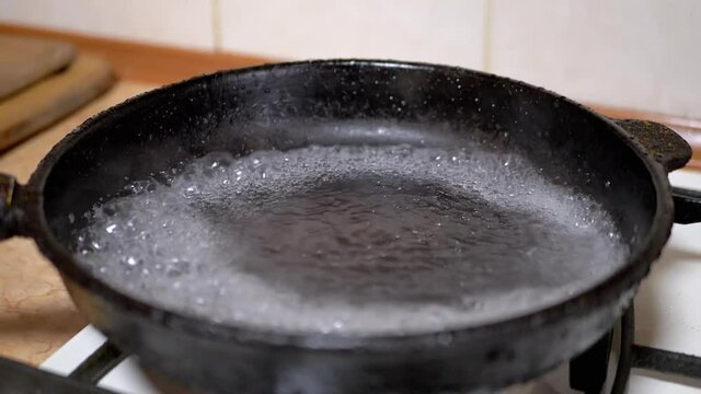 Pouring Water from Glass in Hot, Greasy Skillet. Boiling Liquid, Evaporation