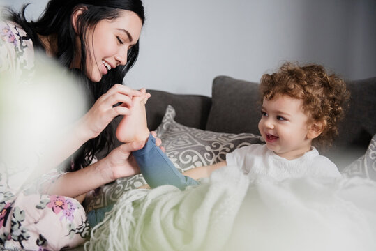 Caucasian mother sitting on sofa playing with toes of son