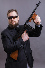 Mature man in sunglasses dressed in suit with tommy gun