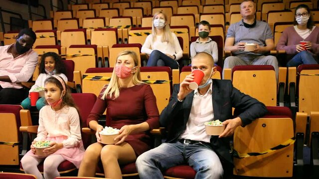 caucasian family in mask sitting at premiere in cinema mother, father and their children sitting at film in auditorium during epidemic. High quality FullHD footage