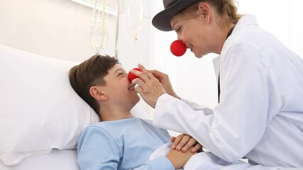 Doctor pediatrician clown with red nose and happy child patient lying in hospital bed, cheers up loneliness with alternative therapy