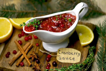 Cranberry sauce in a white gravy boat. Cranberries, cinnamon and spices. Branches of a Christmas tree. Christmas mood.