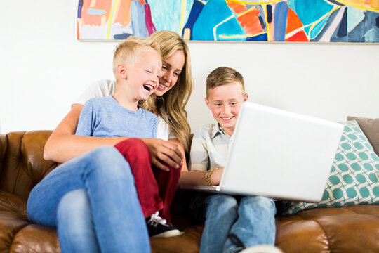 Mother with children (4-5, 6-7) using laptop on sofa