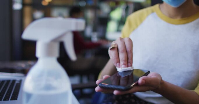 Mid section of african american woman wearing face mask cleaning her smartphone using tissue and dis