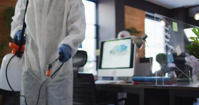 Mid section of health worker wearing protective clothes cleaning office using disinfectant sprayer