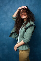 Fototapeta premium young pretty woman with curly brunette hair posing cheerful on blue background, lifestyle people concept