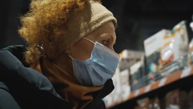 One senior Caucasian woman shopper chooses organic foods for dinner with family during coronavirus quarantine isolation, uses protective gloves and a medical mask, no other people. Theme shopping