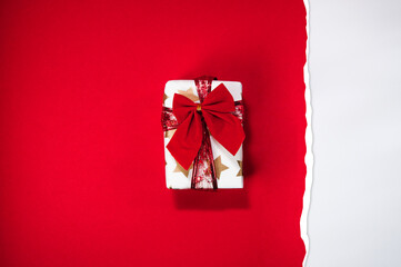 Gift box wrapped with red ribbon on torn red paper, dual red and white color background, flat lay,...