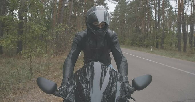 Portrait of confident young Middle Eastern man in motorcycle helmet sitting on black motorbike. Stylish male biker on vehicle on empty spring or autumn road outdoors. Cinema 4k ProRes HQ.